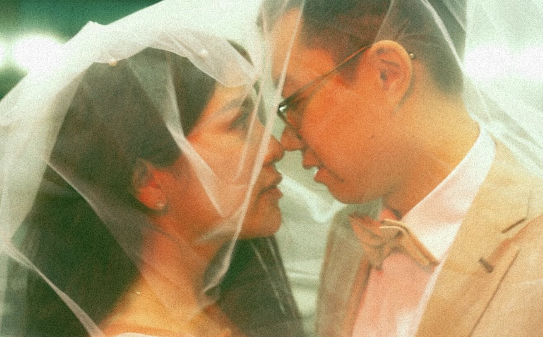 A couple photographed close, beneath a veil